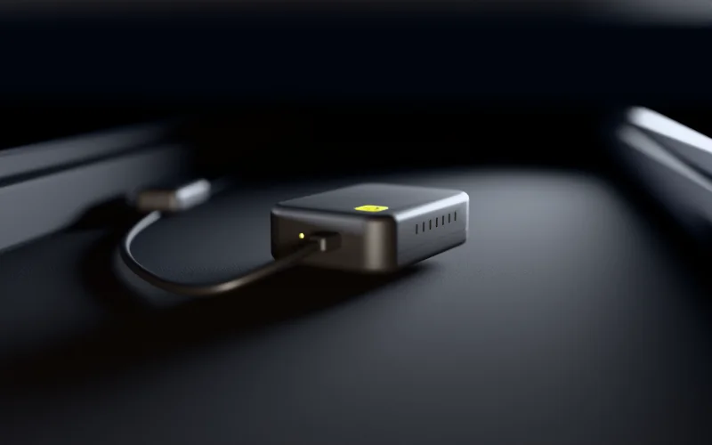 Illustration: the Dashivo Hub Custom on the carpet under a car seat, between the seat rails, with its status light on and its power lead running back to the hardwire kit.